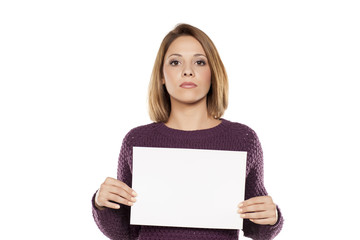 Naklejka premium young serious woman holding a blank sheet of paper for advertising