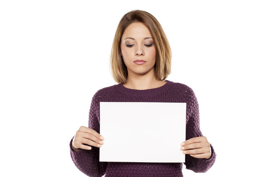 Young Serious Woman Holding A Blank Sheet Of Paper For Advertising