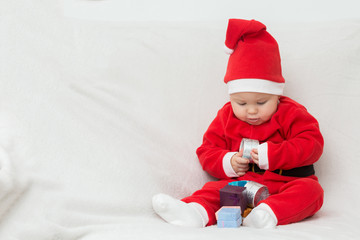 Seven months old baby girl in Santa Claus dress sitting on a whi