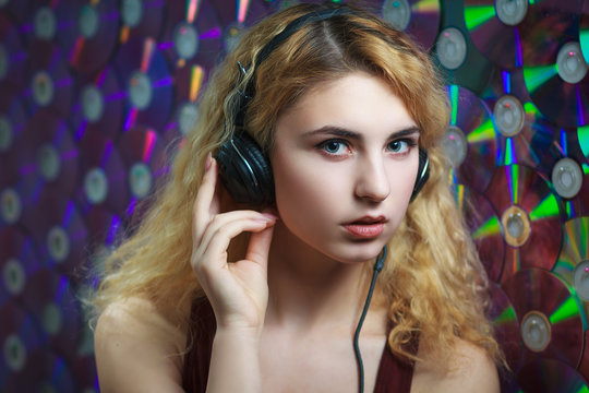 Concept: hipster lifestyle, relaxation. Beautiful young woman in headphones have fun and listen music with colorful CD's on background.