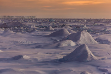 Rough ice landscape in Antarctica during sunset with iceberg