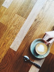 Having cup of latte or cappucino indoor cafe, wooden table