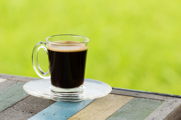 hot black coffee on wooden table with green nature background