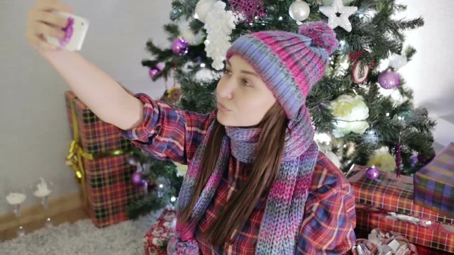 Young beautiful girl doing selfie near the Christmas tree.