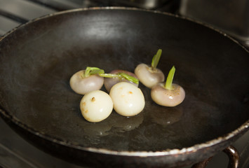 Fresh organic baby turnips, in a metal frying pan, to be cooked and caramelised.