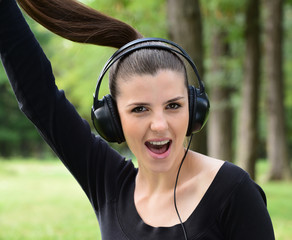 Young happy surprised woman with headphones listening to music outdoors in the park
