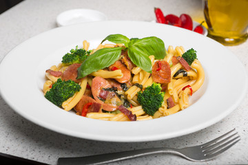 A delicious fresh gourmet Italian strozzapreti pasta dish, with pancetta, italian sausage, broccoli, vegetables, topped with fresh basil.