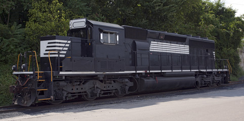 Black diesel train engine against trees. Horizontal.