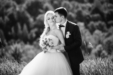 Fototapeta na wymiar Black and white. Young couple in love, groom and bride in wedding dress kissing at the nature. Wedding. Wedding day. Bridal bouquet.