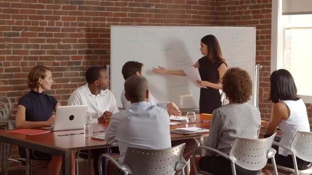 Businesswoman At Whiteboard Giving Presentation In Boardroom