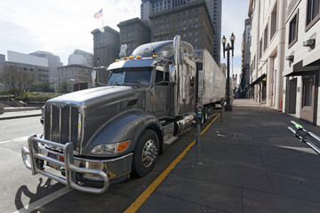 Side view of gray semi cab and trailer parked on urban street. Nobody. Horizontal.