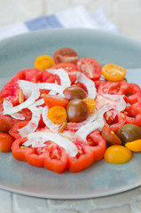 A vibrant healthy mixed tomato, mozzarella, pine nut and balsamic vinegar salad, served on a rustic plate on a tile table.