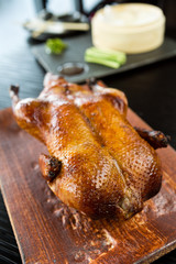 A beautiful roasted, free range, crispy golden oriental peking duck, served on a rustic wooden cutting board, ready to be sliced.
