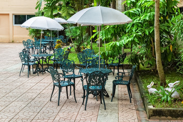 Fototapeta na wymiar Patio with Tables and Alloy chairs under Umbrella in Garden