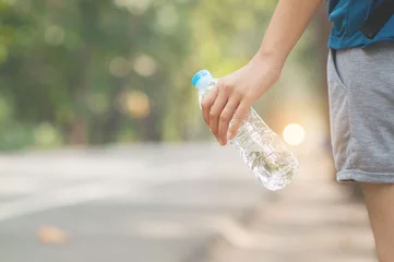 Poster Woman hitchhiker hand holding bottle of water on nature background. © eggeeggjiew