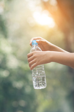 Close up woman hand holding bottle of water on nature background with sunlight.
