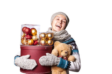 Young cute smiling girl in sweater, holding a box of Christmas decorations. Winter, Cristmastime, New Year holiday.