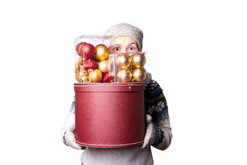 Young cute smiling girl in sweater, holding a box of Christmas decorations. Winter, Cristmastime, New Year holiday.