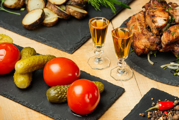 Fried meat, potatoes, vegetables on black slate plates and two shot glasses with cognac