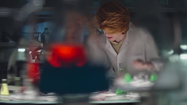 Tracking shot of senior professor showing something in Petri dish to young student in laboratory while woman looking through microscope