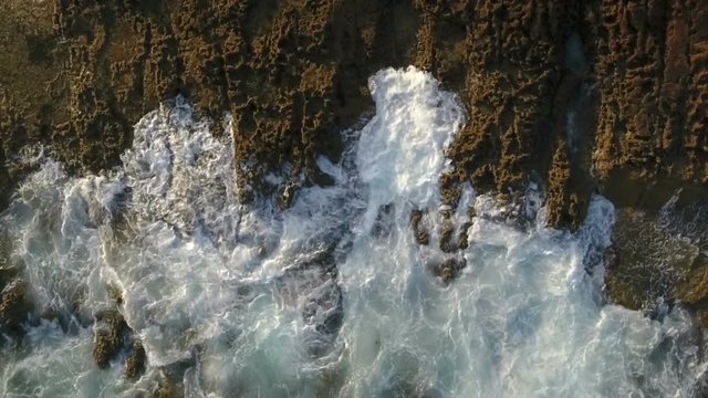Aerial. Movements of waves splashing on the rocks, view from the sky.
