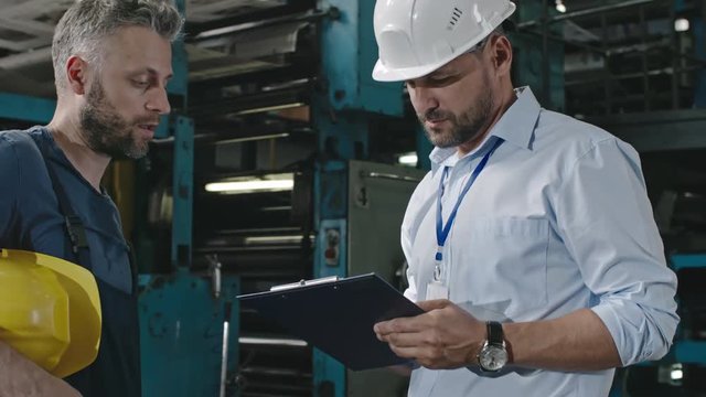 Exhausted factory laborer discussing work with supervisor making notes, then agreeing and shaking hands