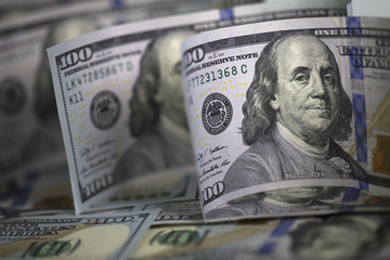 Row of three lightly curved hundred us bills standing on hundred us banknotes background. Focus on first banknote President Franklin's face, shallow depth of field.  Horizontal image.