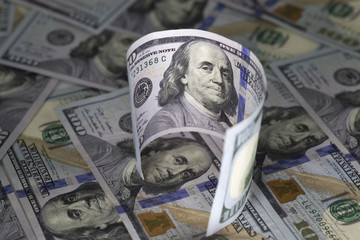 Curved hundred us dollar banknote standing on hundred us dollar bills background.