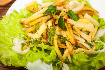 Fried potatoes on a white plate with herbs on wooden background. The view from the top