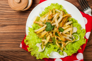 Fried potatoes on a white plate with herbs on wooden background. The view from the top