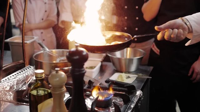 Chef's Masterclass. Chef Cooking With Fire In Frying Pan.
Professional Chef In a Commercial Kitchen Cooking Flambe Style.
