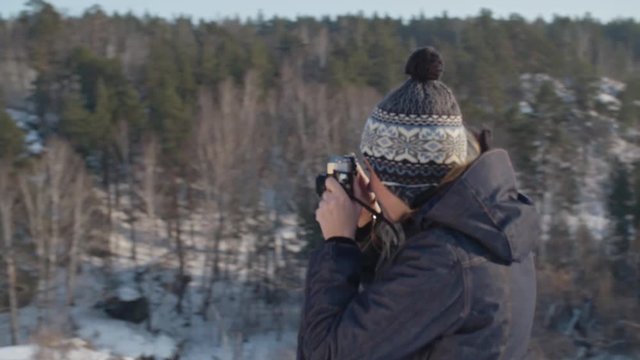 PAN of young woman taking picture with analog camera of husband holding fussy toddler boy during winter trip
