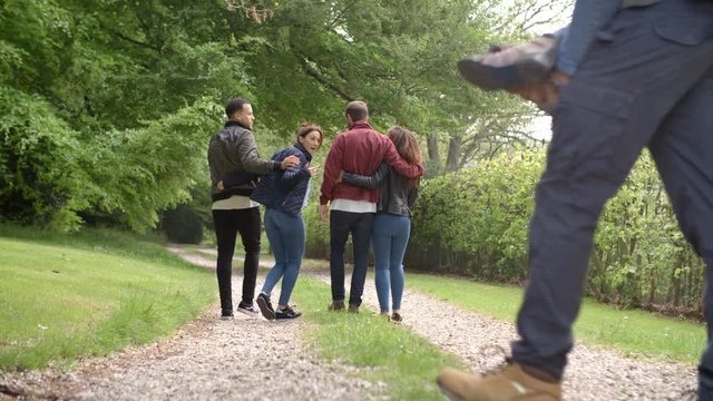 Young couples walk and piggyback in country lane, back view