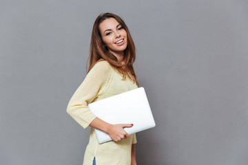 Portrait of a smiling brunette woman standing and holding laptop