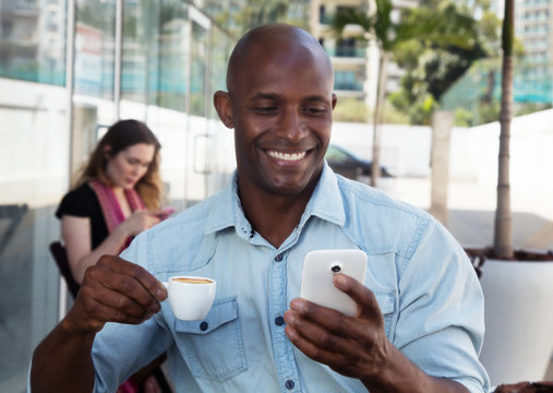 Lachender Afrikaner schreibt Nachricht mit Handy im Restaurant