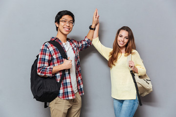 Smiling interracial students standing with backpacks and giving high five