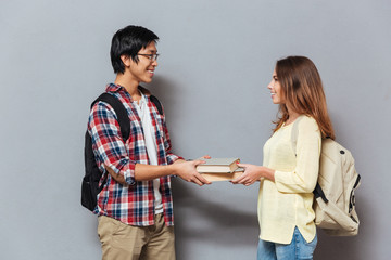 Smiling interracial student couple with backpacks exchanging books