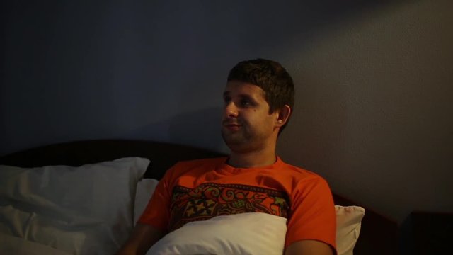 Man watching TV at night. A man lying on the bed. The guy switches the TV remote control.