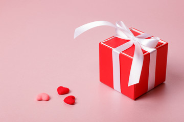 Valentine day composition: red gift box with bow and small hearts on light pink background.