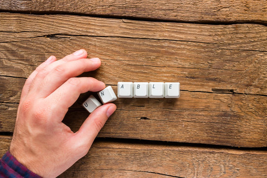 man changes the word unable to able of the keyboard keys on a wooden background