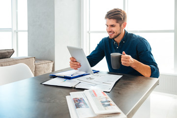 Happy man holding tablet in hand and drinking coffee