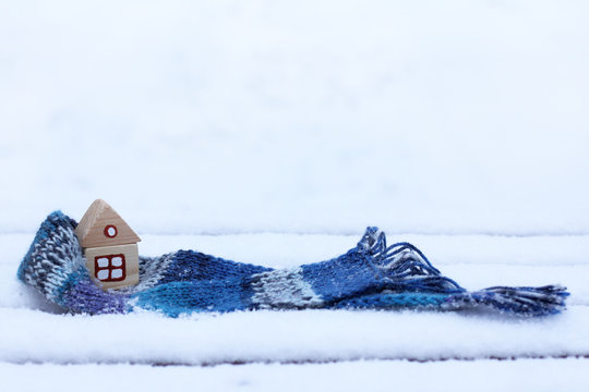  warming things for comfort/ small wooden house wrapped in a scarf on the background of snowy landscape 