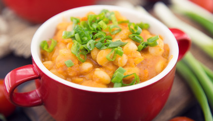 White beans in tomato sauce in a red ceramic bowl on rustic wood