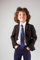 Little boy smiles sweetly bowing his head looking up. Gray background.