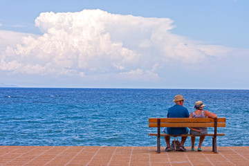 A copy of seniors sitting on a bench at sea shore