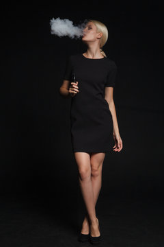 woman in a black dress smokes an electronic cigarette