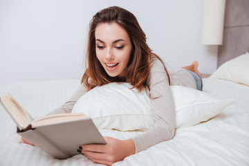 Beautiful young woman lying on bed and reading book