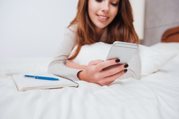 Woman lying on bed with phone and texting a message