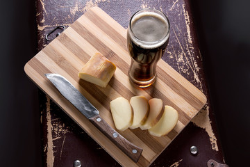 Glass with dark beer with smoked cheese on cutting board.