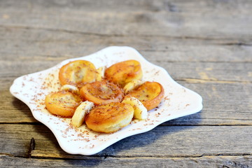 Fried battered banana decorated with chocolate and fresh sliced bananas. Simple delicious fried bananas in batter on a plate isolated on old wooden background. Tasty and healthy breakfast idea